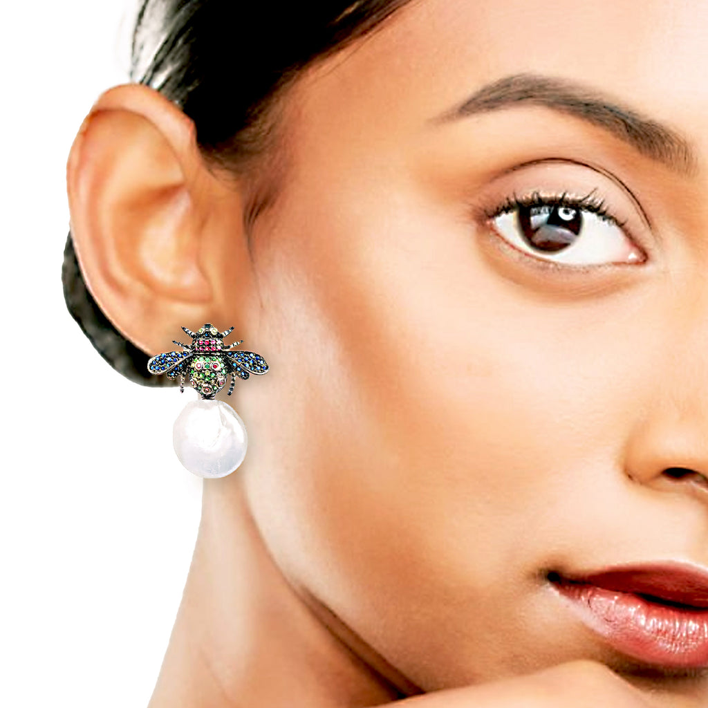 Close-up of a woman wearing an earring with a bee design and pearl drop.