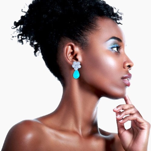 Woman wearing a turquoise teardrop earring with a white flower design on a white background